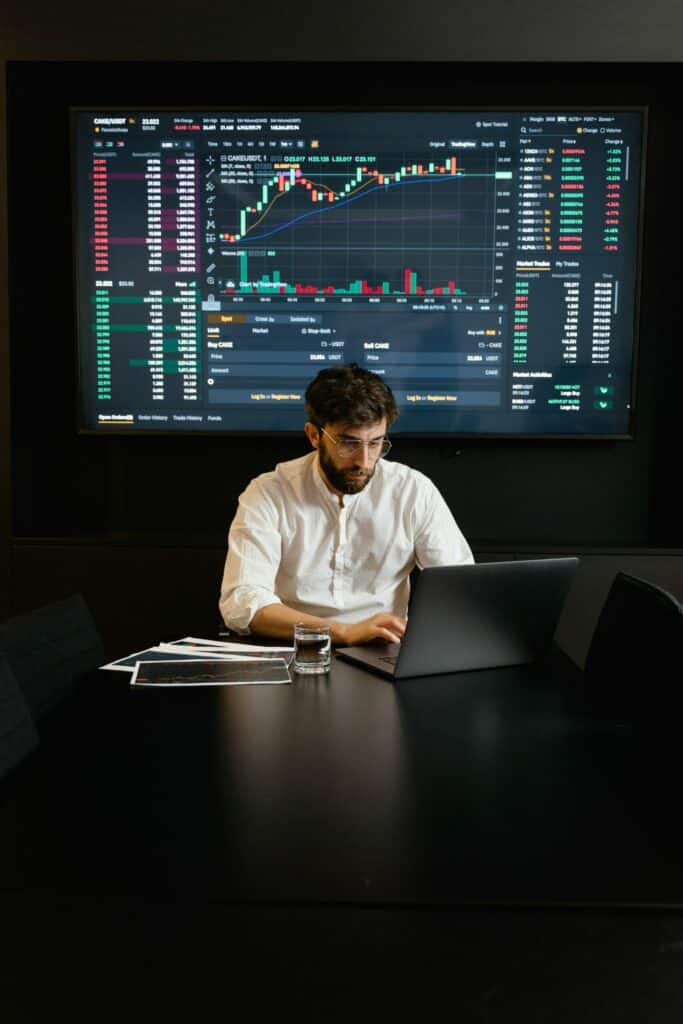 Man on computer with data viz on large screen